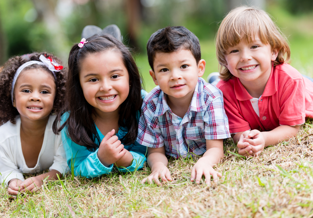 Four smiling preschool children lying on the grass